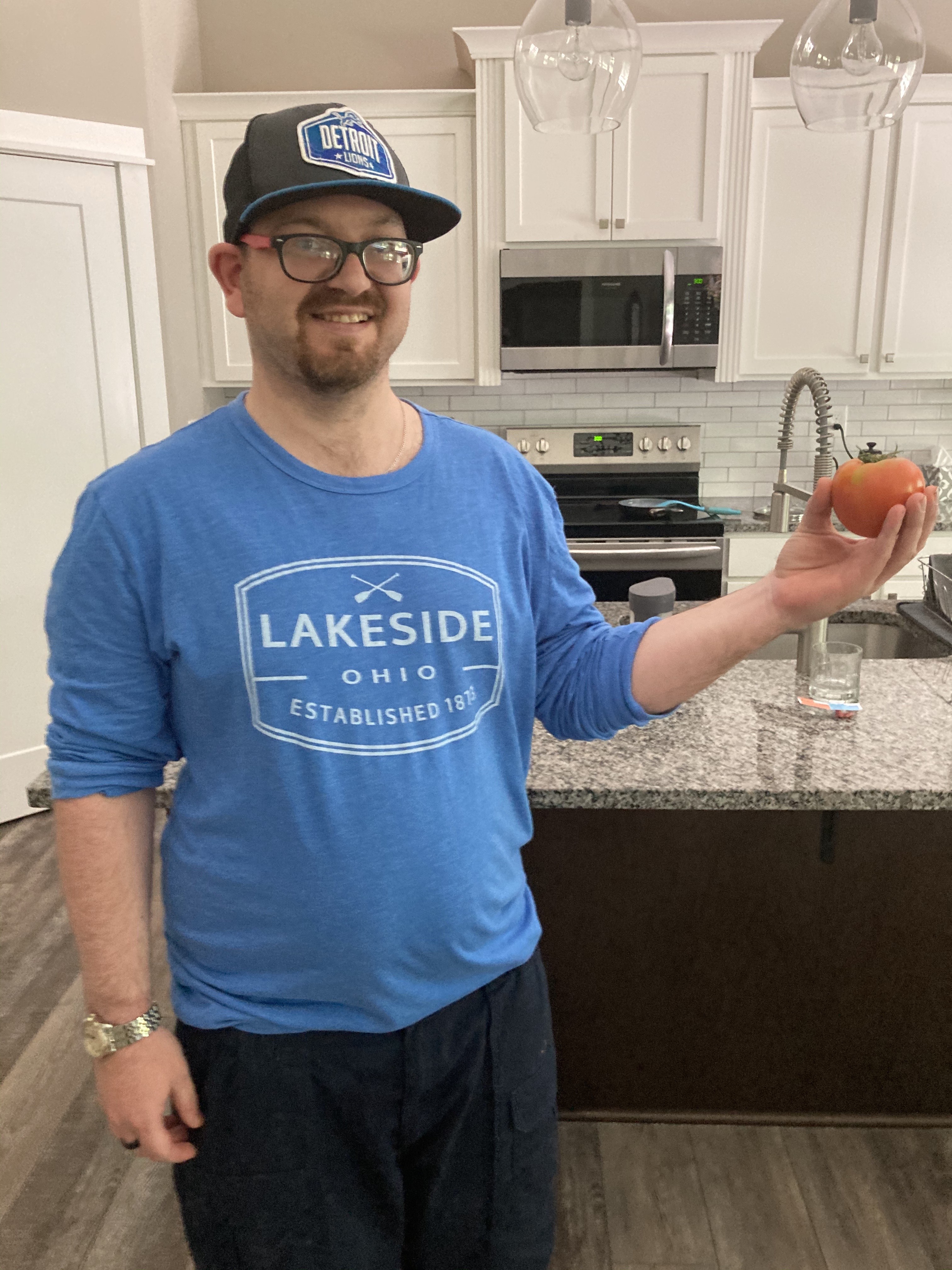 Chris holding the first tomato of the season from our garden.